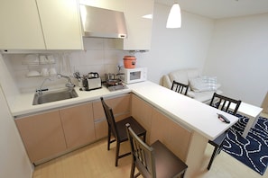 A compact kitchen with a sink, stove, microwave, and a dining area with chairs and a table. - Galleria Palace 1 (Seoul)