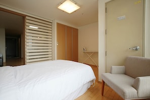 A hotel room with a bed, a chair, a wardrobe, and a door. - Galleria Palace 2 (Seoul)
