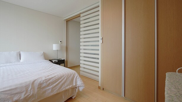 A bedroom with a bed, a nightstand, a lamp, and a sliding door closet. - Galleria Palace 2 (Seoul)