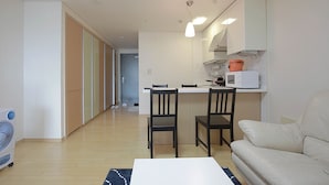 A modern kitchen with white cabinets, a microwave, and a dining area with two chairs and a table. - Galleria Palace 2 (Seoul)