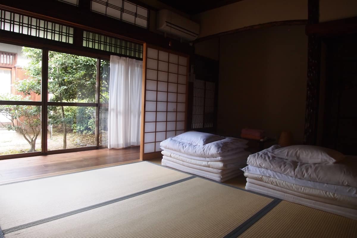 A traditional Japanese room with tatami flooring, a sliding shoji screen, and a view of a garden.