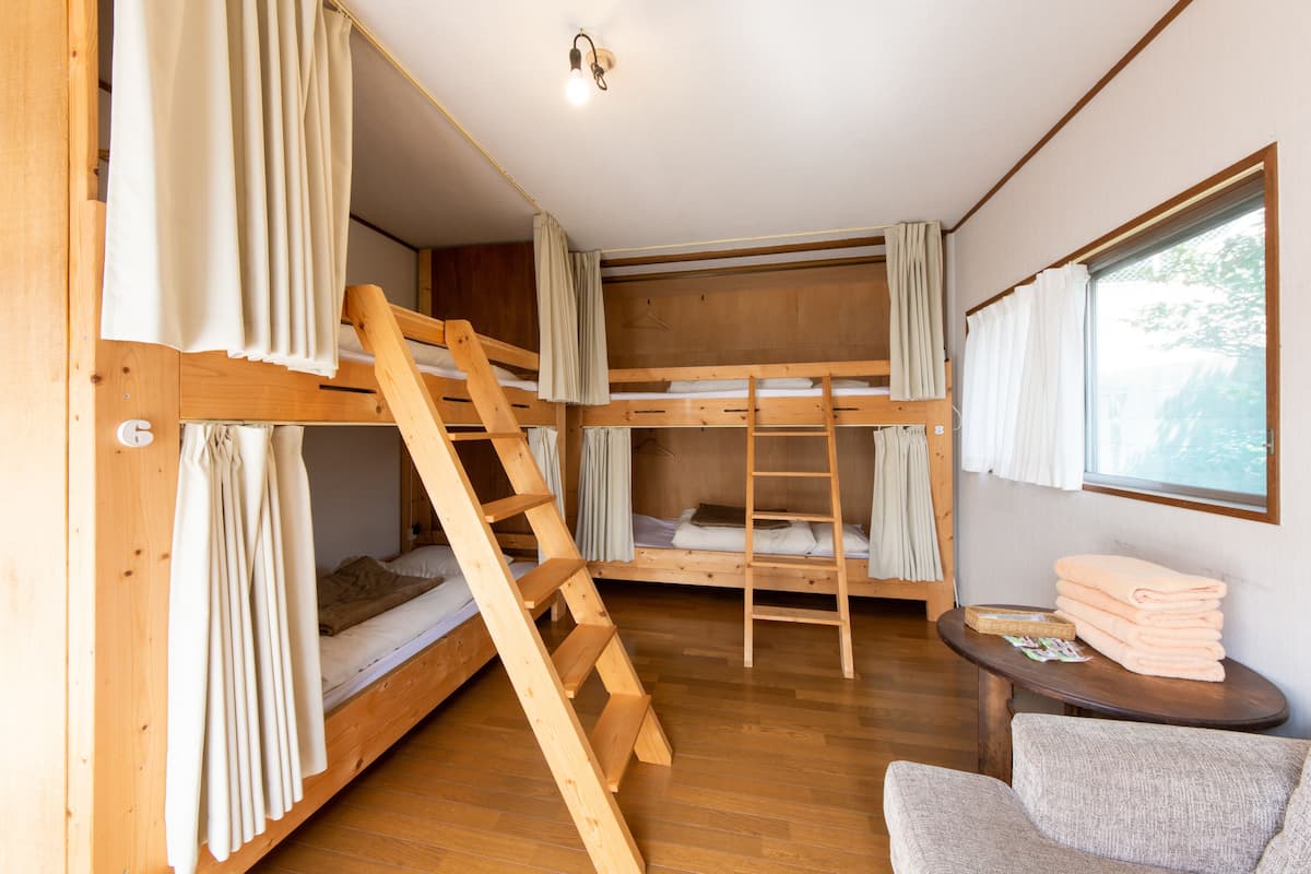 A bunk bed room with a wooden ladder, a small table with towels, and a window with curtains.