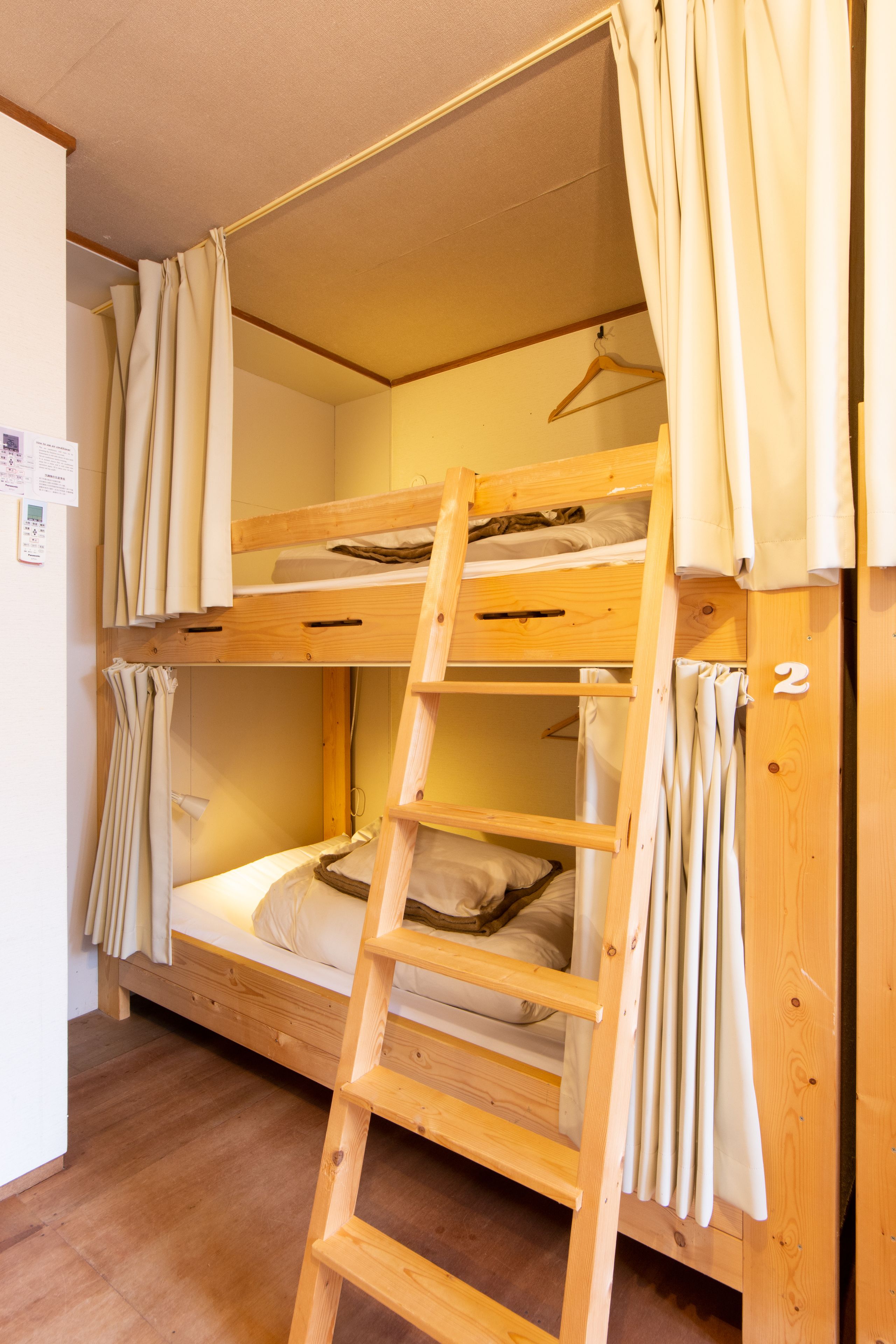 A bunk bed room with a wooden ladder, curtains, and a wooden hanger.
