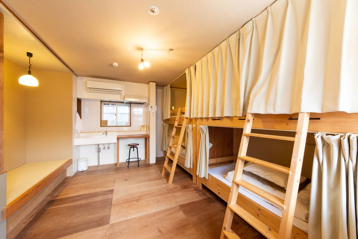 A dormitory room with bunk beds, a small kitchenette, and a wooden floor.