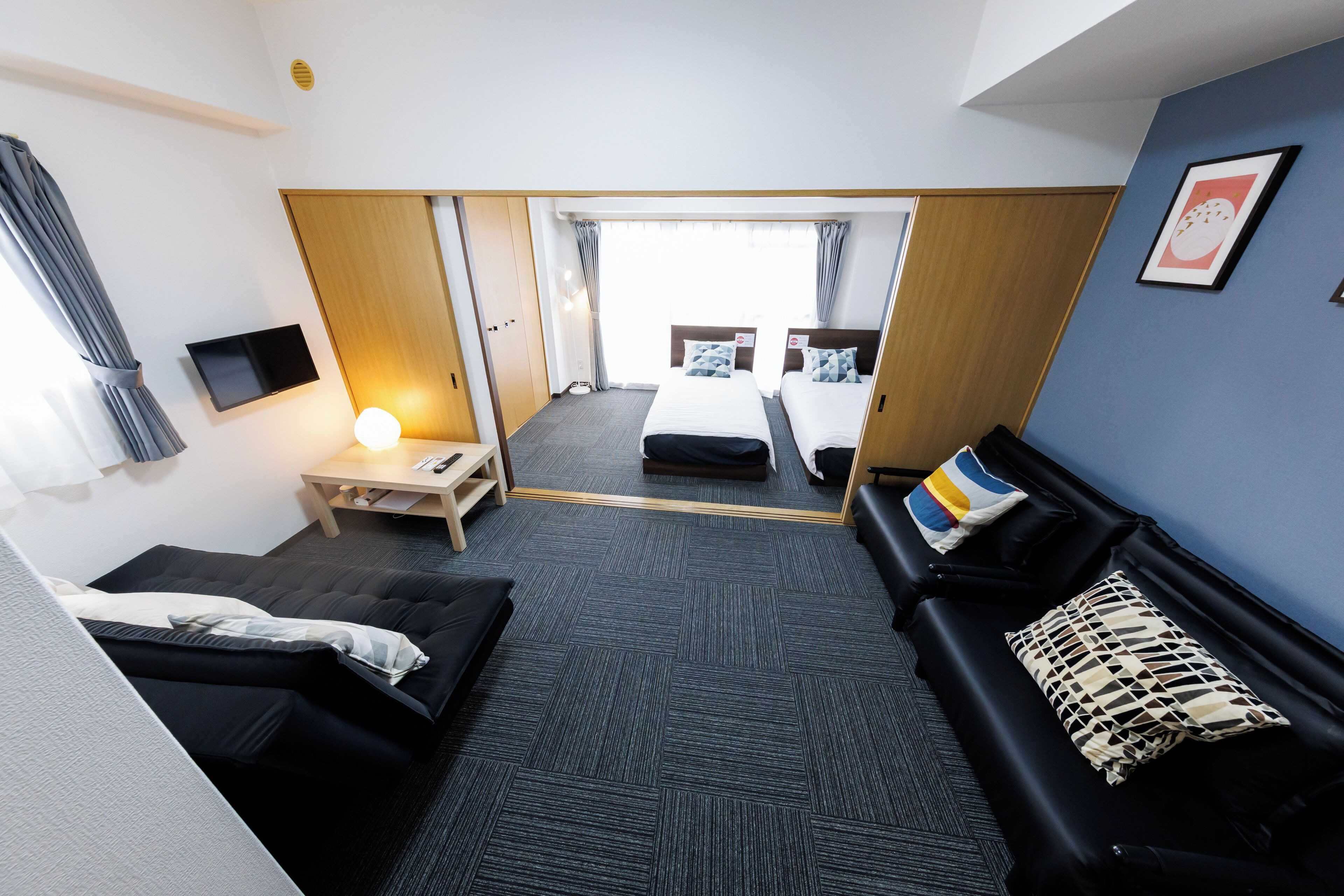 A hotel room with a sofa, a bed, a desk with a lamp, and a TV.