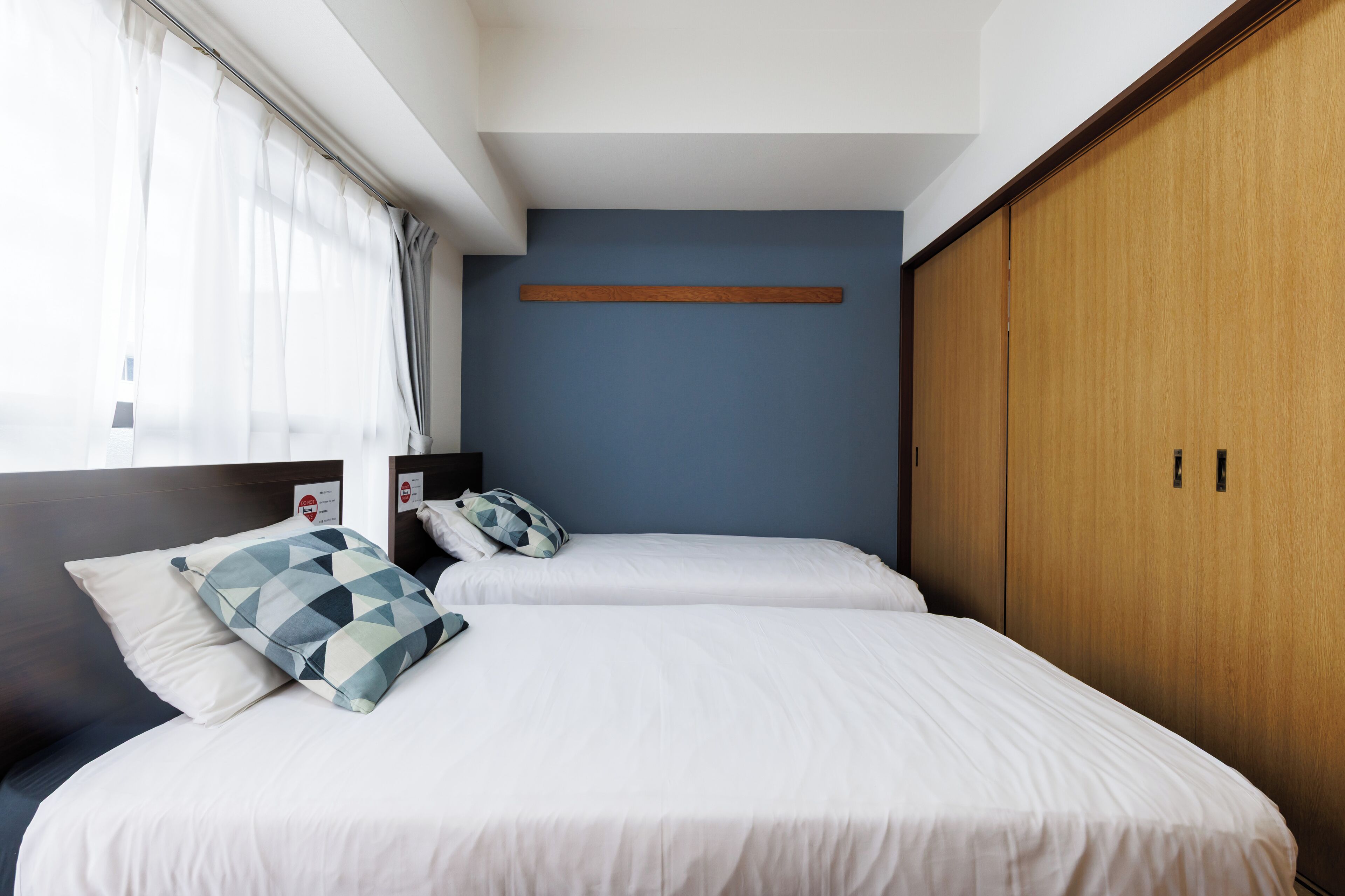 A hotel room with two beds, a wooden wardrobe, and a blue accent wall.