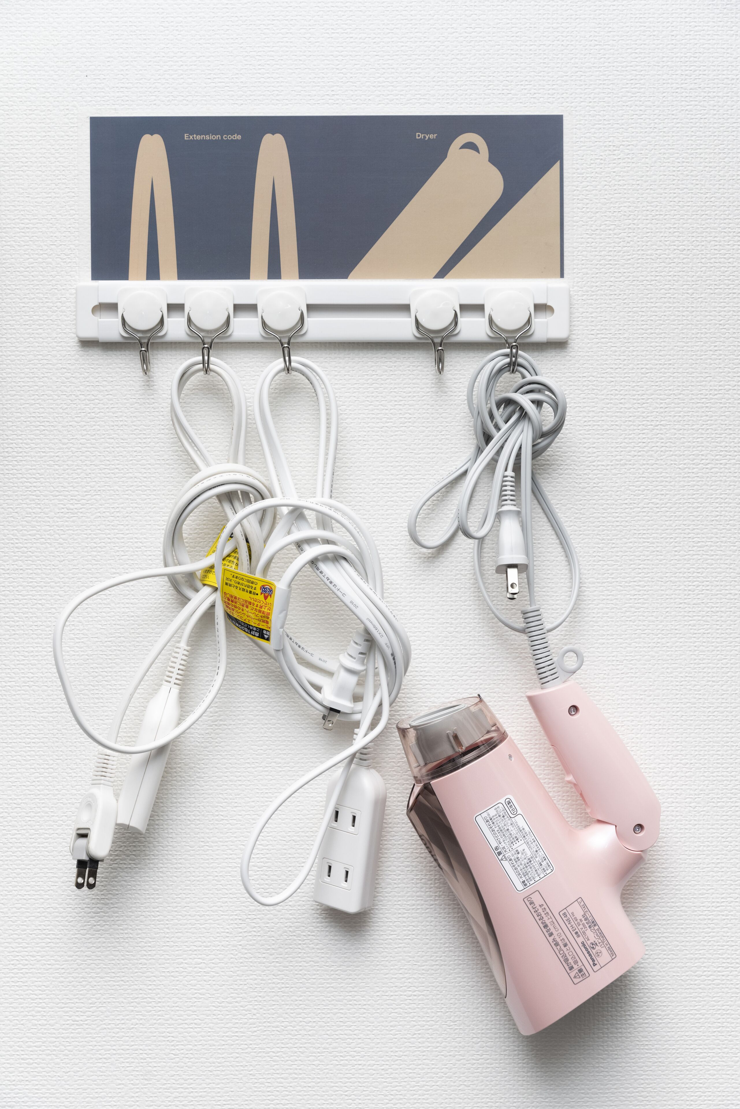 A wall-mounted extension code holder with various white and pink power cords and adapters.