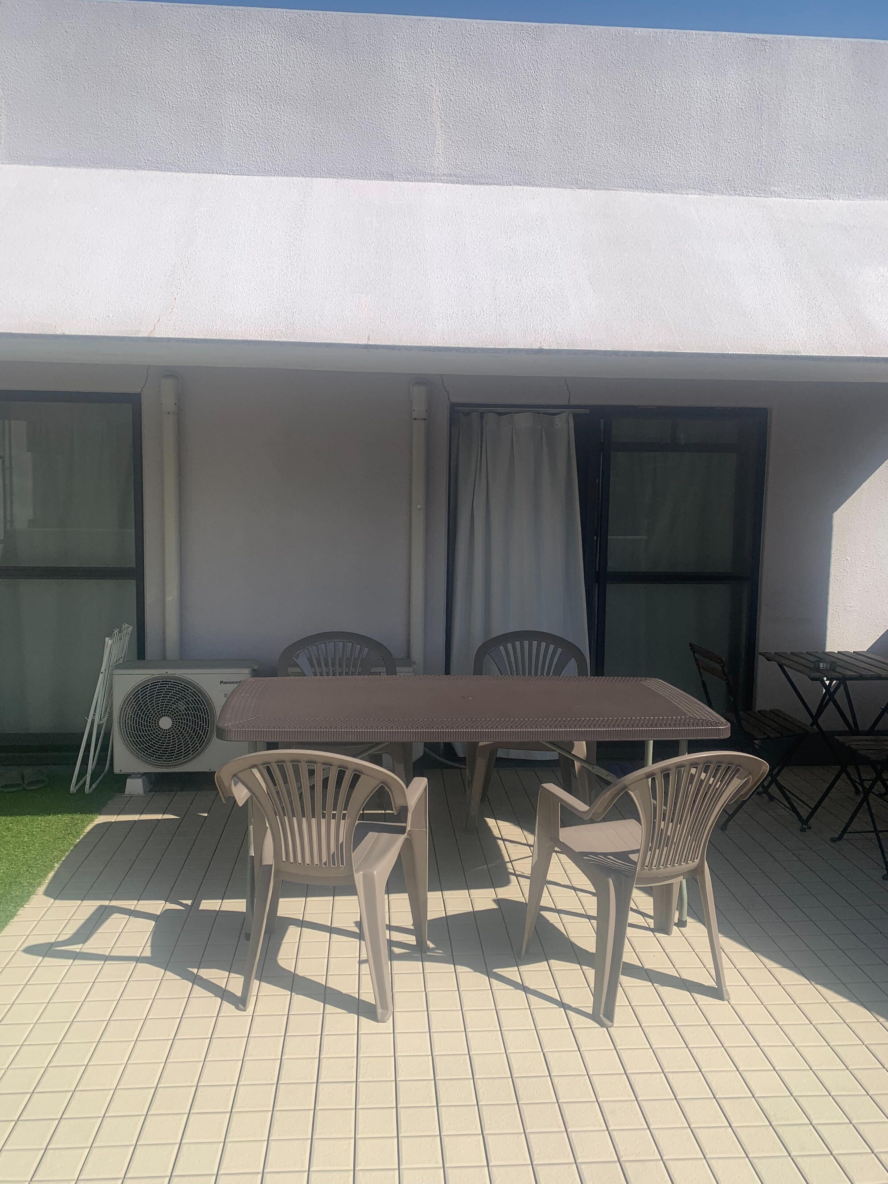 Une terrasse extérieure avec une table et des chaises, un appareil de climatisation et une fenêtre avec des rideaux.