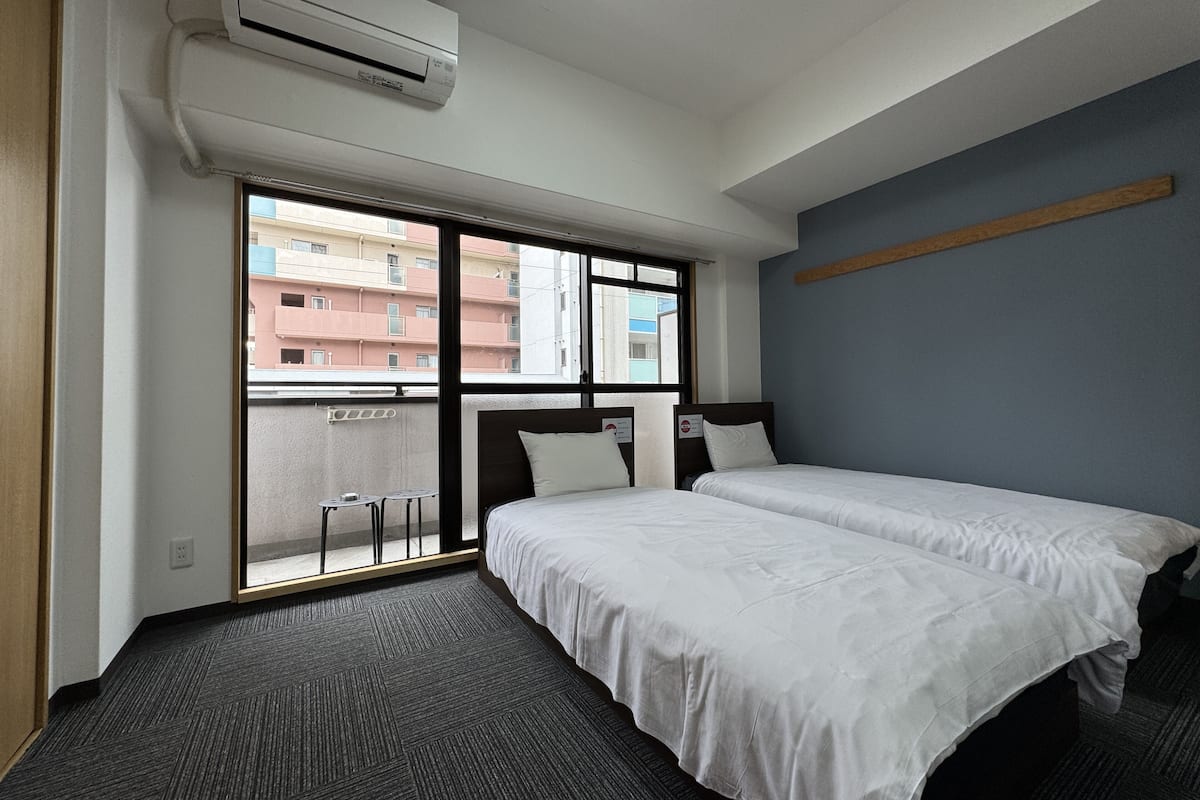 A hotel room with two beds, a large window, and an air conditioning unit.