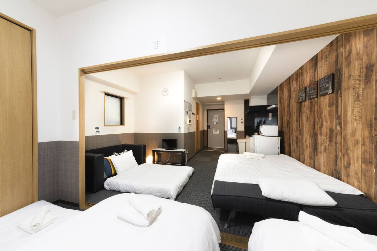 A hotel room with three beds, a wooden accent wall, a clock, and a television.