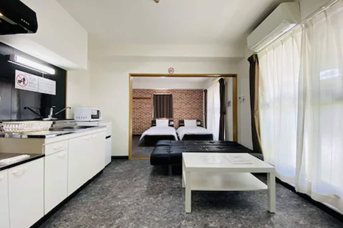 A compact hotel room with a kitchenette, a bed, a small table, and a bathroom visible through an open door.