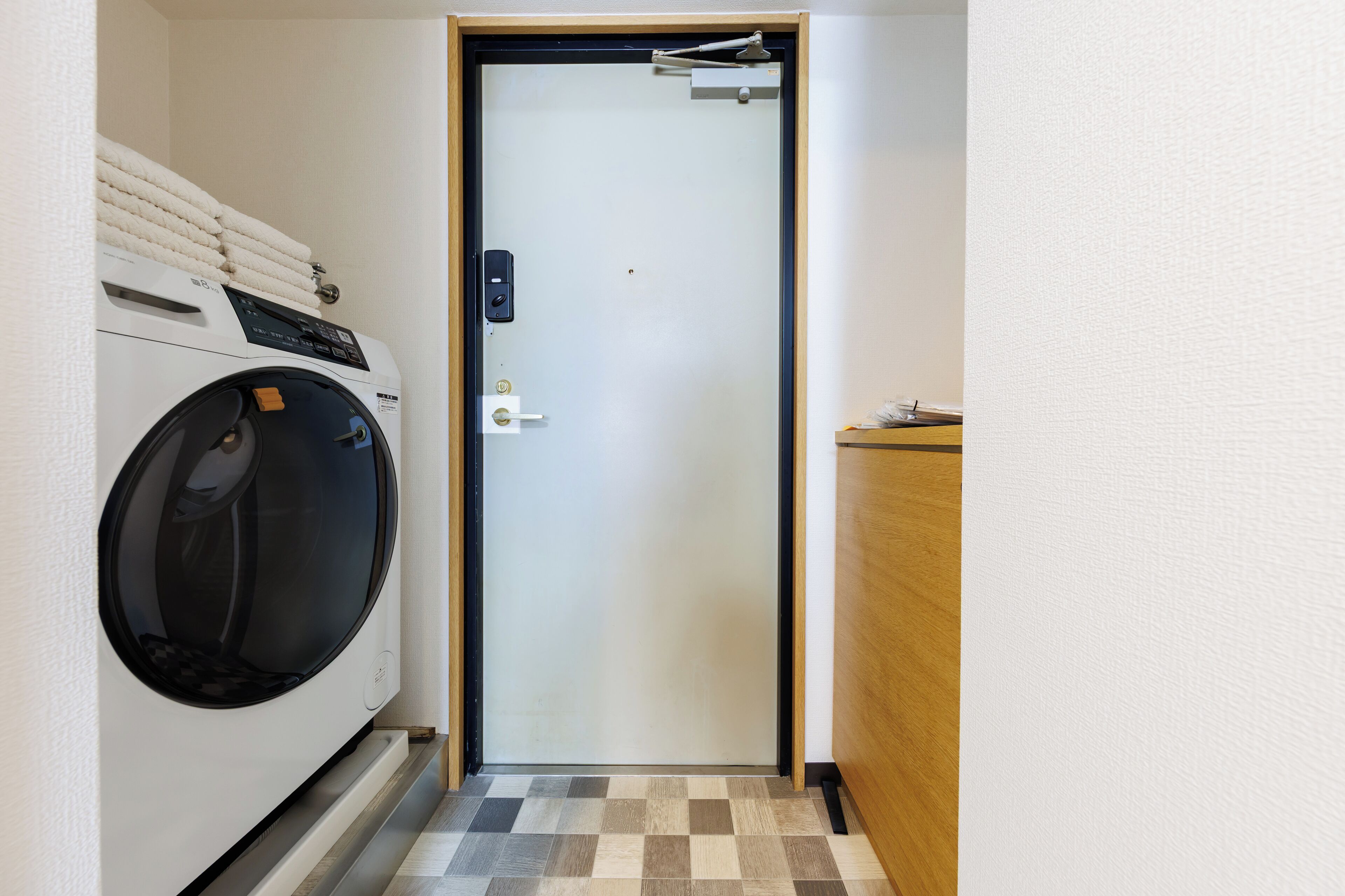 A laundry room with a front-loading washing machine, a door with a handle, and a checkered floor.