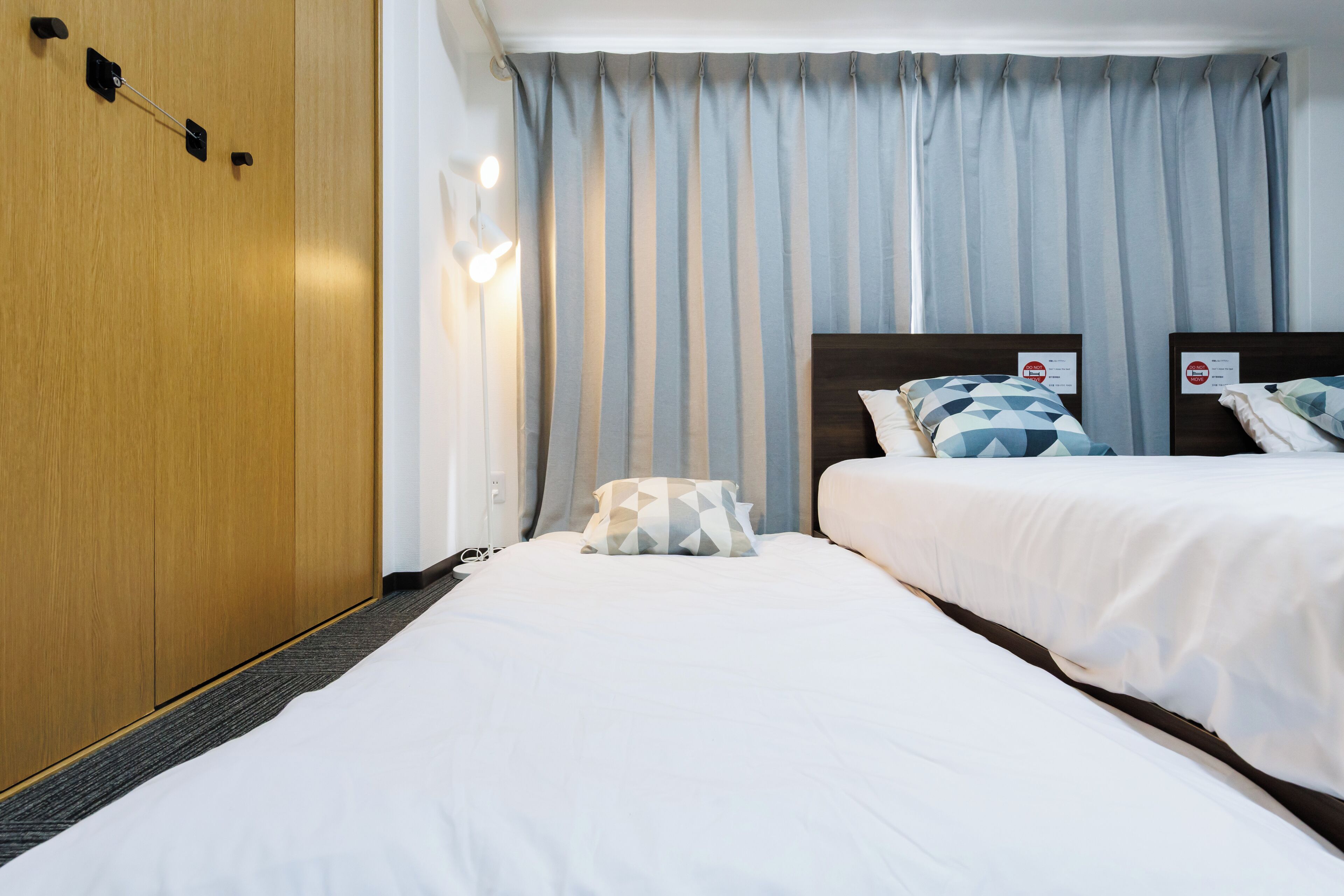 A hotel room with two beds, a wooden wardrobe, a striped curtain, and a sign on the wall.