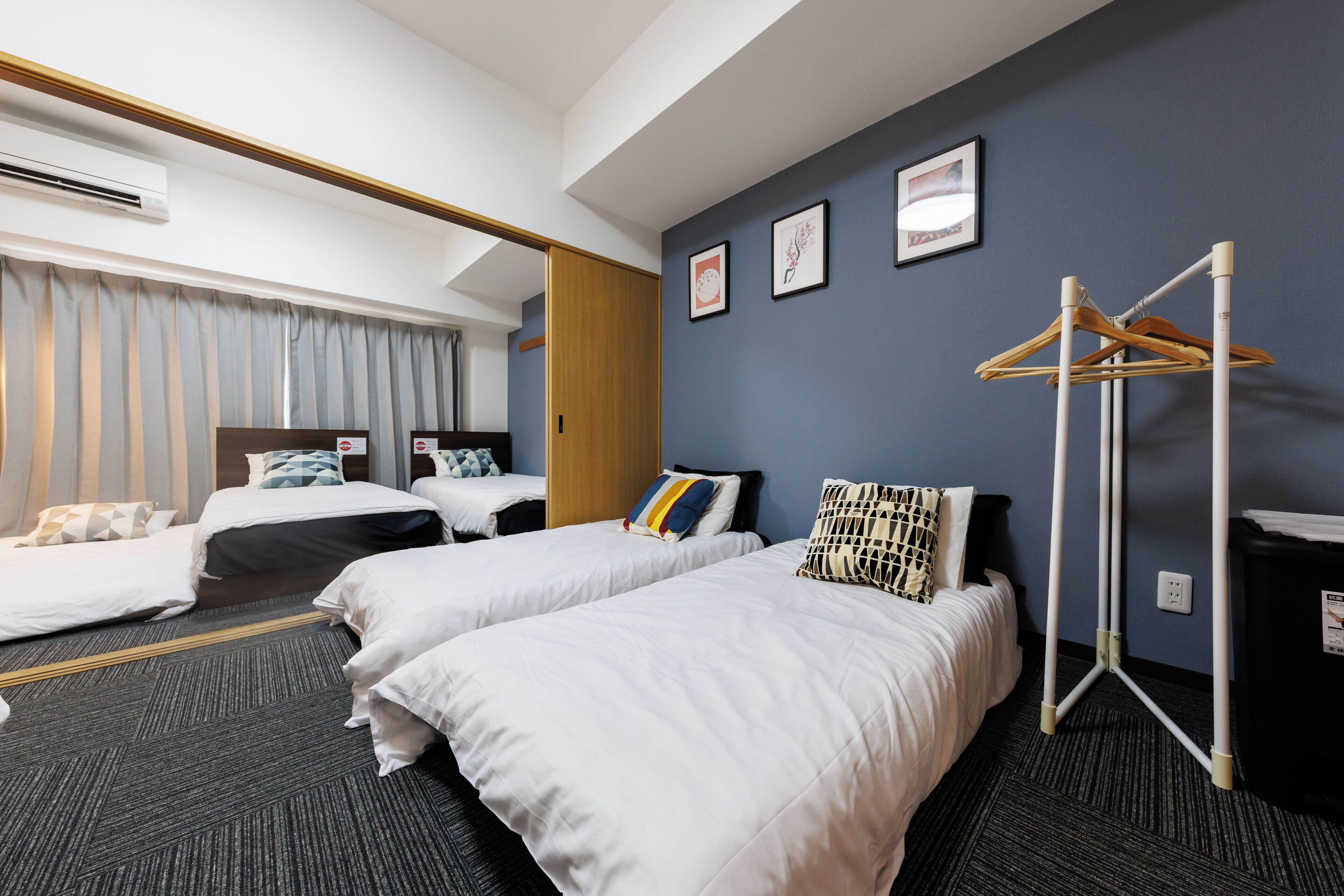 A hotel room with two beds, a wooden wardrobe, a drying rack, and a framed picture on the wall.