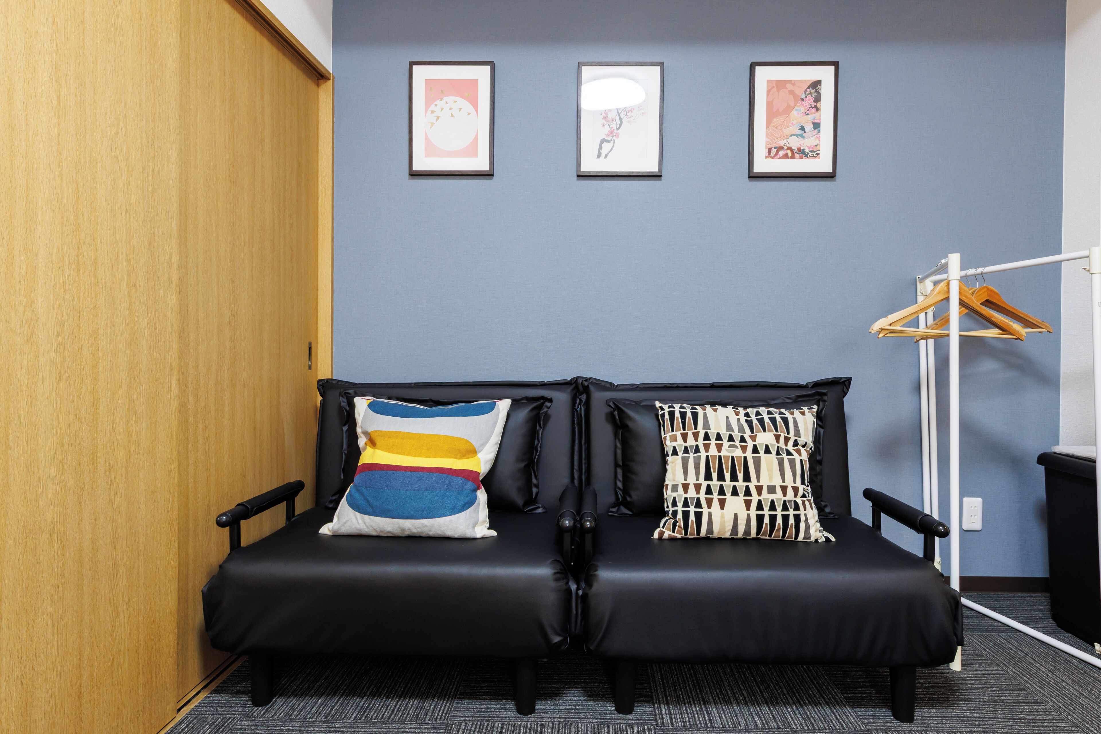 A room with a black sofa, two pillows, a wooden wardrobe, and three framed pictures on the wall.
