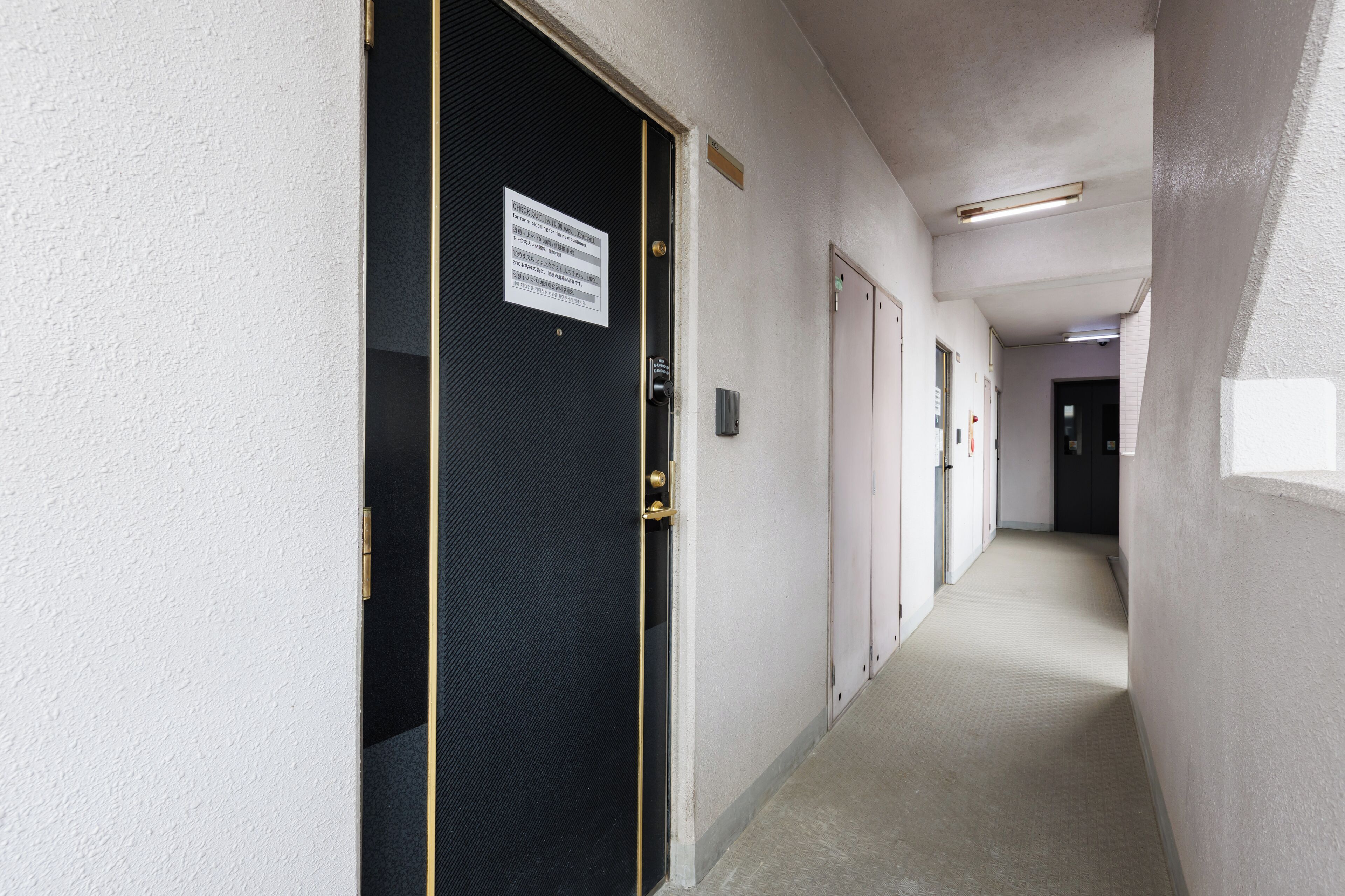 Un couloir avec une porte fermée, un panneau sur le mur et un luminaire.