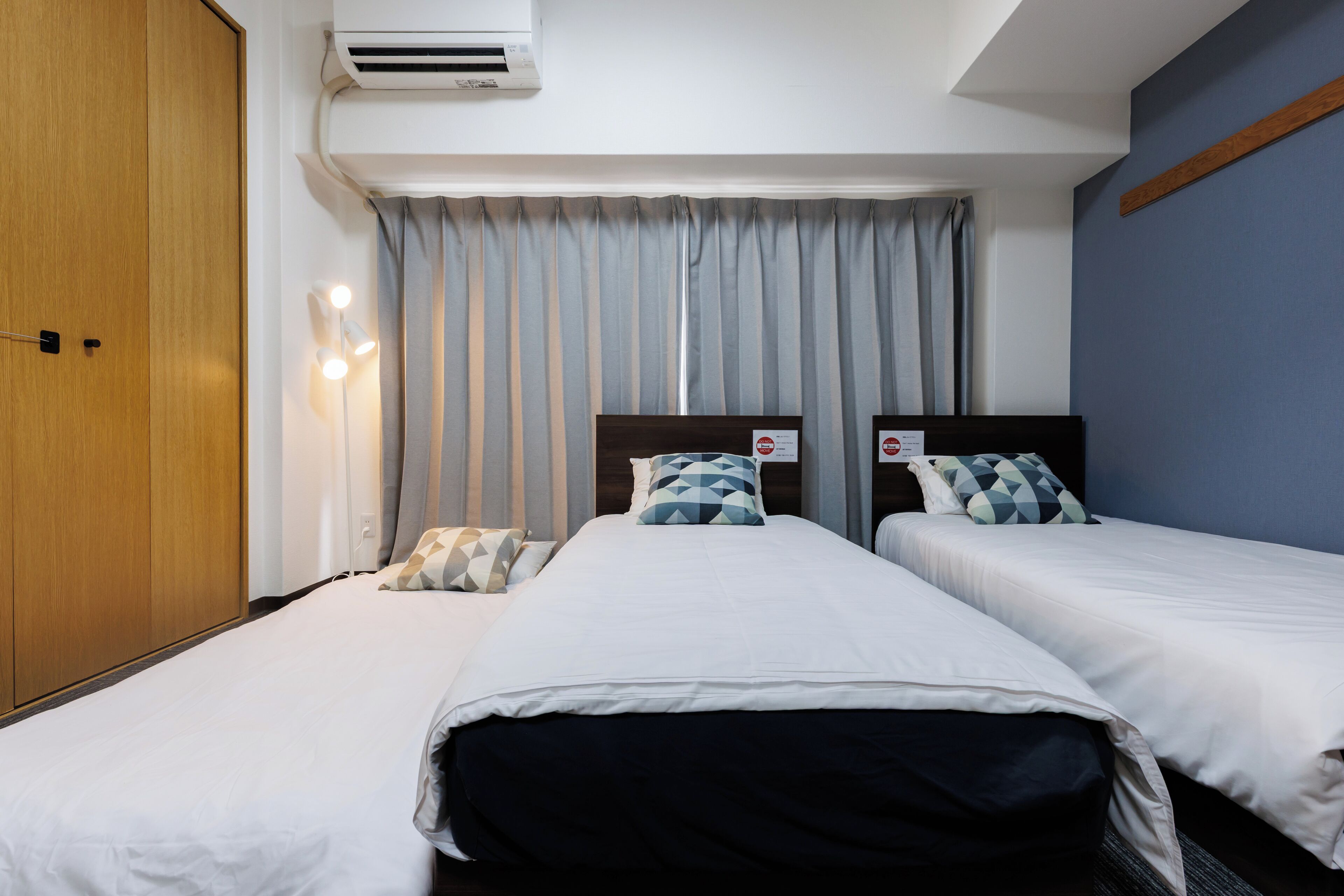 A hotel room with two beds, a wardrobe, an air conditioner, and a curtain.