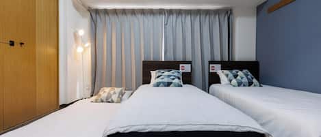 A hotel room with two beds, a wardrobe, an air conditioner, and a curtain.