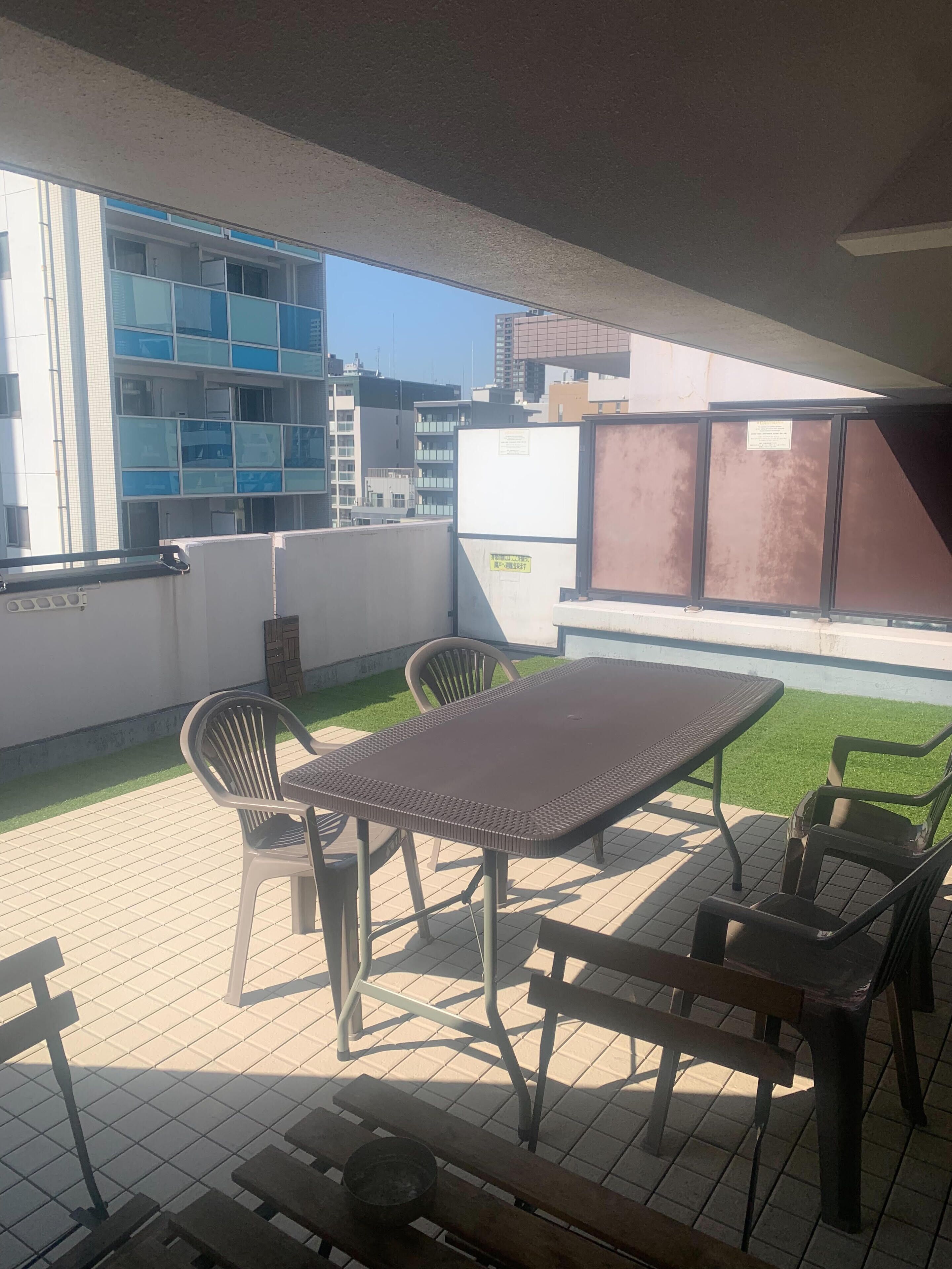 A patio with a table and chairs, a small garden area, and a view of buildings in the background.