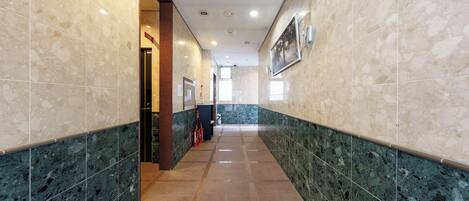 A hallway with marble walls and a tiled floor, leading to a door at the end.