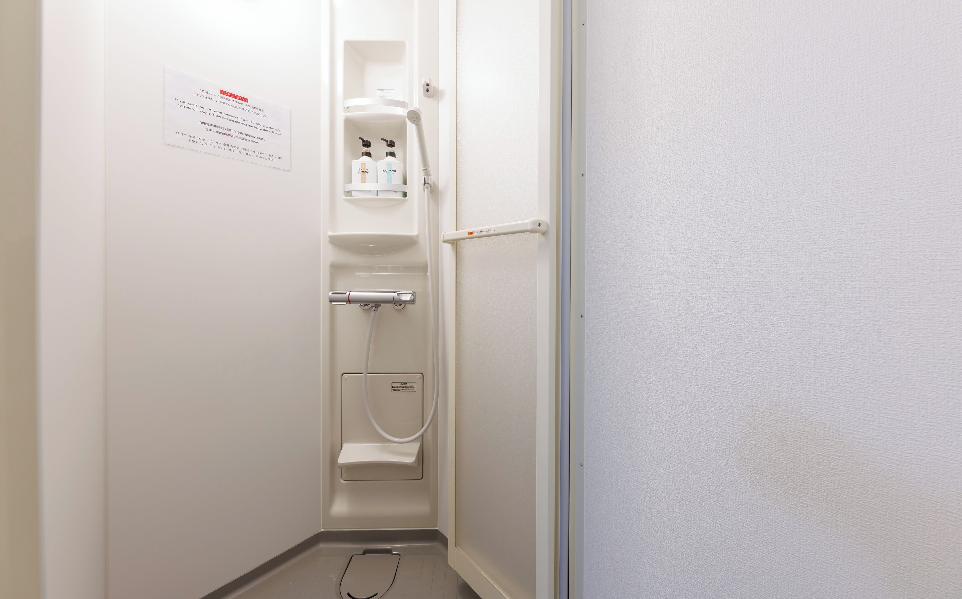 A bathroom with a toilet, a shower, and a sink. There is a caution sign on the wall.