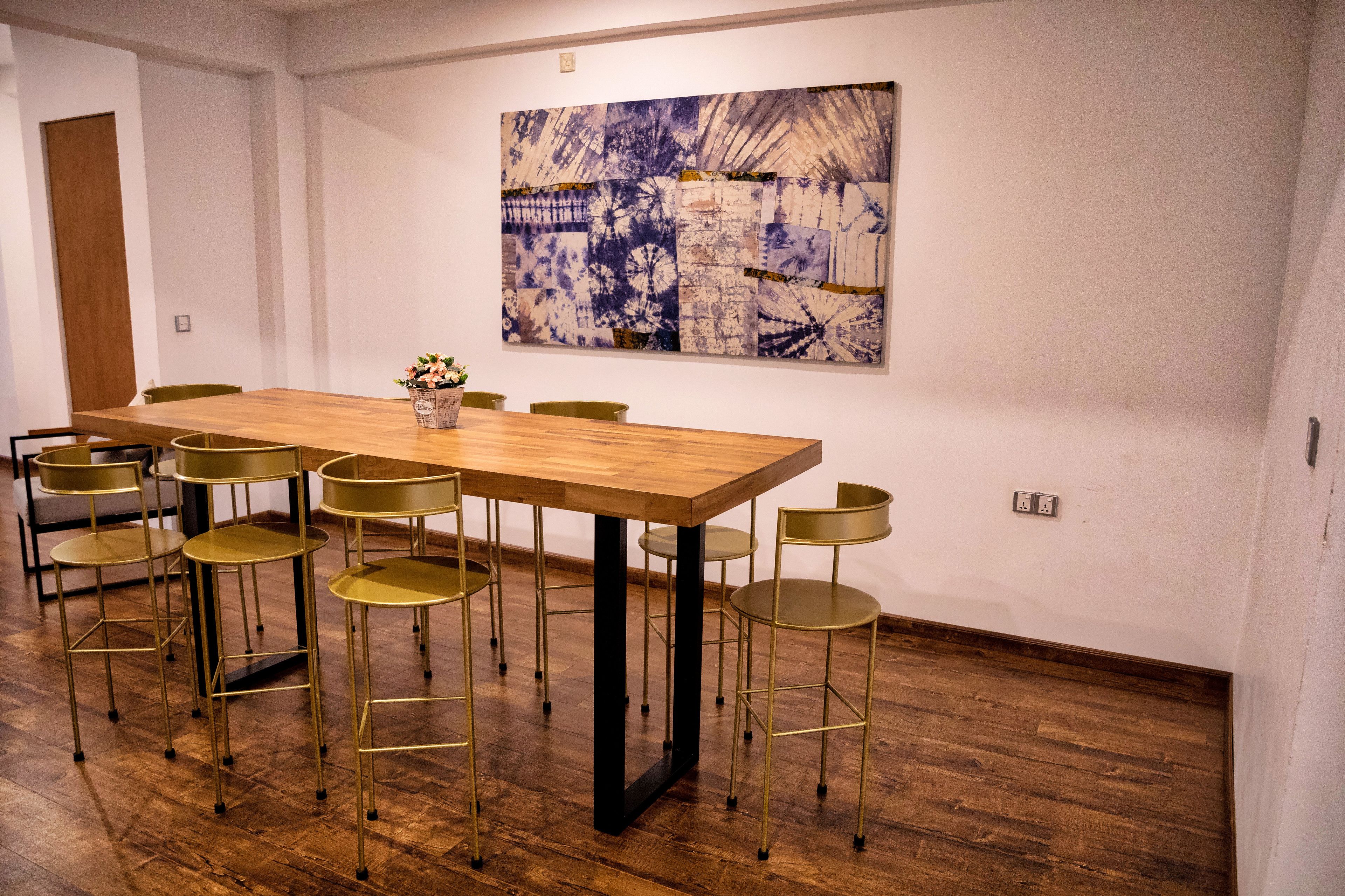 A conference room with a wooden table, six gold chairs, and a large abstract painting on the wall.