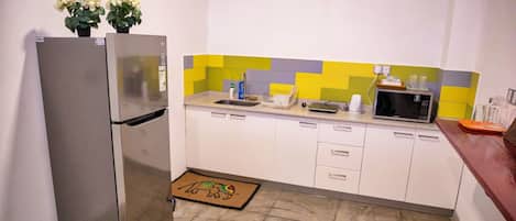 Una cocina compacta con un refrigerador de acero inoxidable, un microondas y un lavamanos.