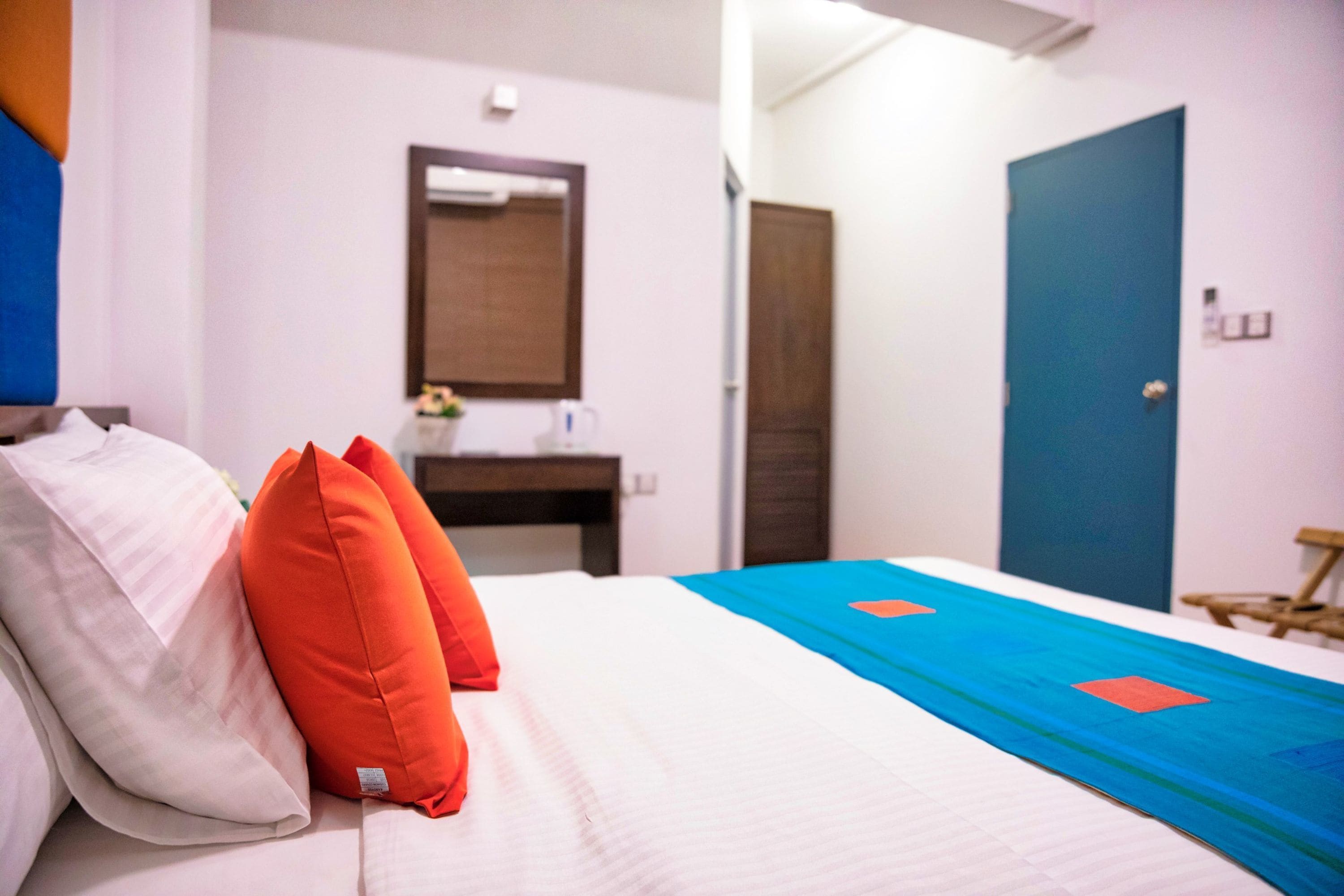 Habitació d'hotel amb llit, almoines, una tauleta de nit, un mirall, una porta blava i una cadira de fusta.