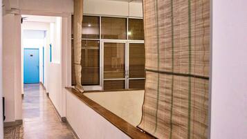 A hallway with a wooden floor, a blue door at the end, and a window with a patterned blind.