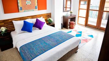 A hotel room with a large bed, a wooden headboard, a desk with a mirror, and a view of the outside through a large window.
