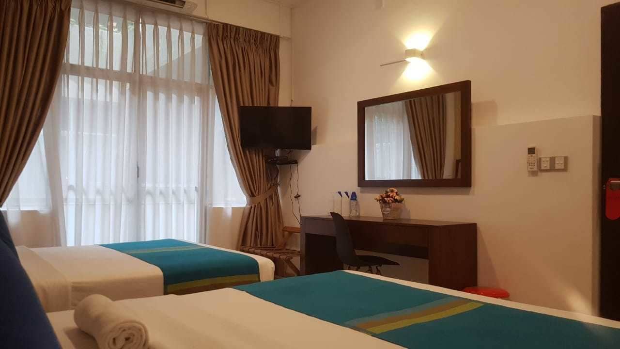 A hotel room with two beds, a desk, a chair, a TV, and a mirror.