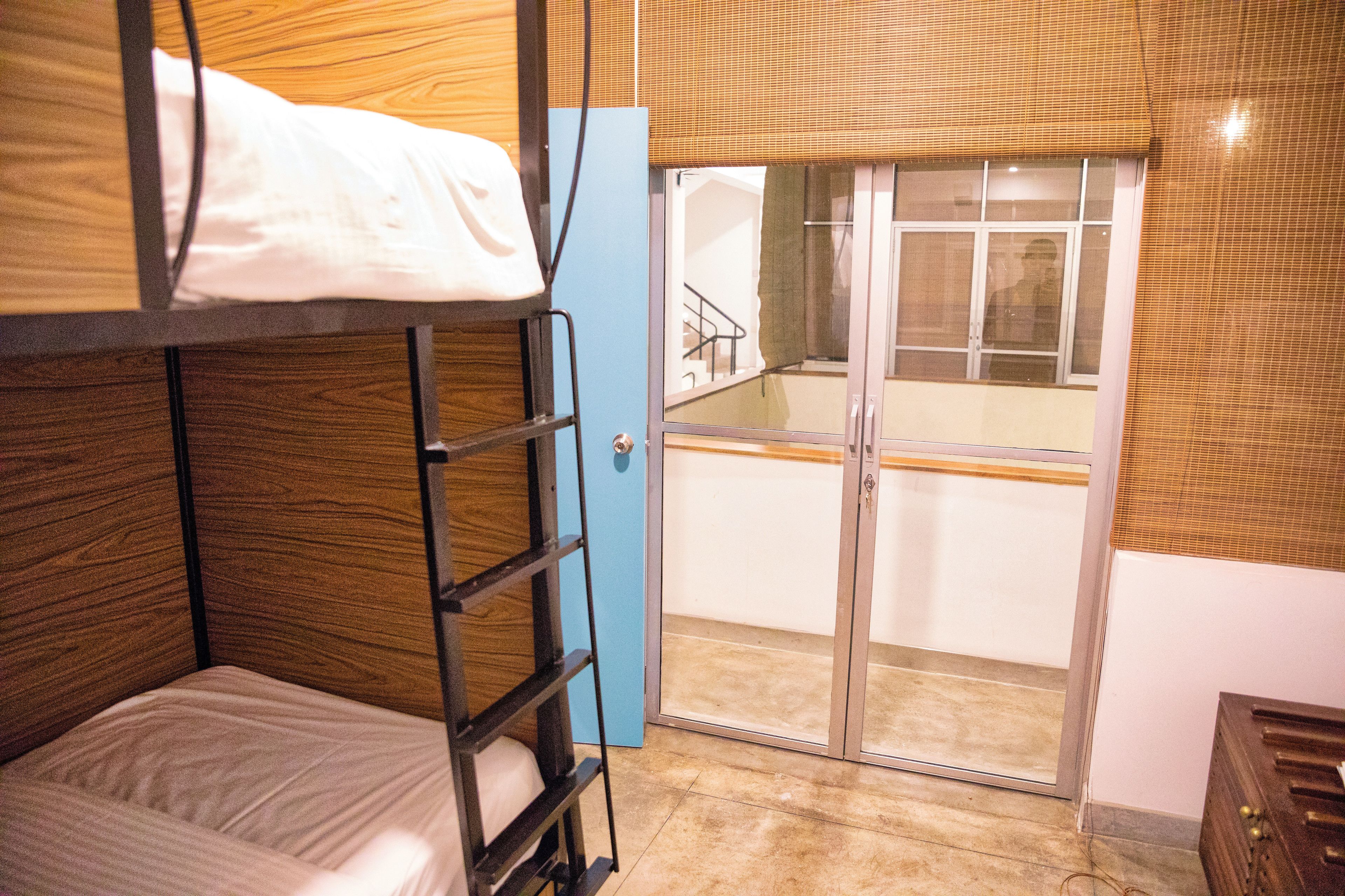 A bunk bed with a ladder, a blue door, and a view of a balcony with a railing.