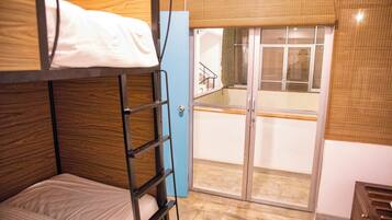 A bunk bed with a ladder, a blue door, and a view of a balcony with a railing.
