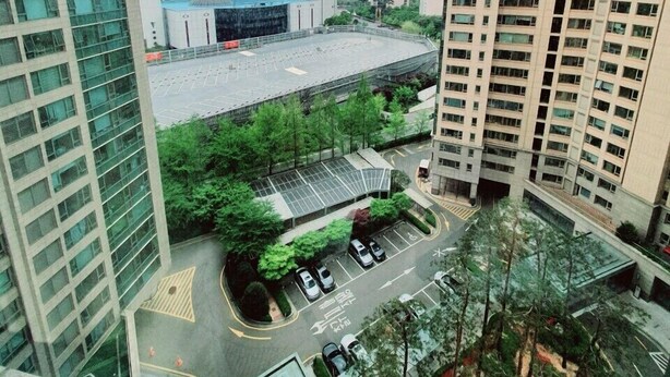 A high-rise building with a parking lot and a large building in the background. - Galleria Palace 3 (Seoul)