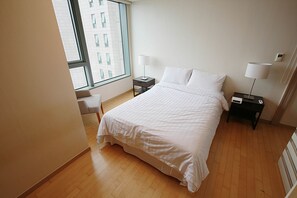 Quarto de hotel com uma cama grande, duas mesas de cabeceira com abajures, uma janela com vista para um prédio e um radiador no chão.