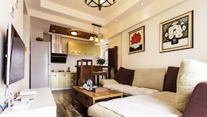 A modern living room with a sofa, a coffee table, and a TV. There is a kitchen in the background with cabinets and a refrigerator. - Chengdu Tu Le Apartment (Chengdu)