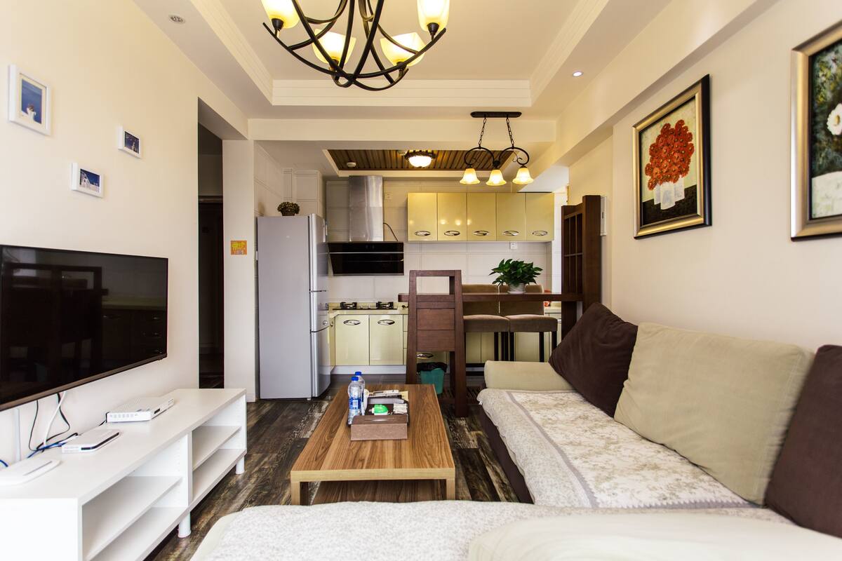Una sala de estar moderna con un televisor de pantalla plana, una mesa de centro de madera, un sofá y una cocina al fondo.