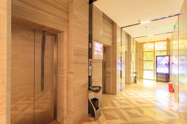 An interior corridor with a patterned floor, a glass wall with a digital display, and a trash bin.