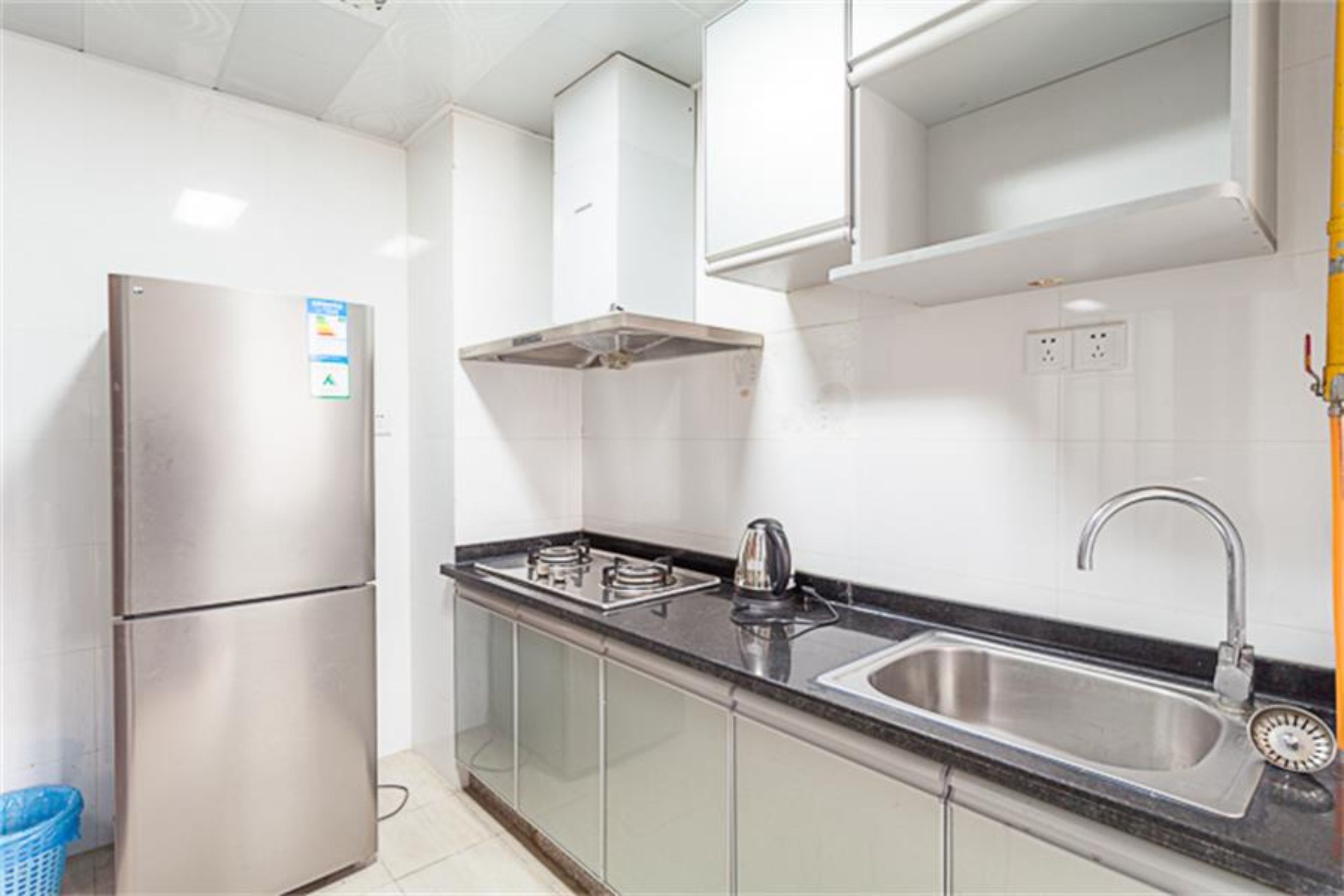 A modern kitchen with a stainless steel refrigerator, a gas stove, a sink, and a blue trash bin.
