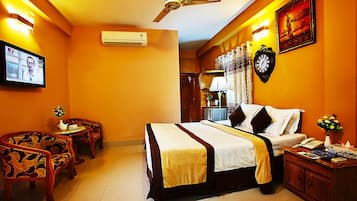 A hotel room with a bed, two chairs, a desk, a clock, and a television.