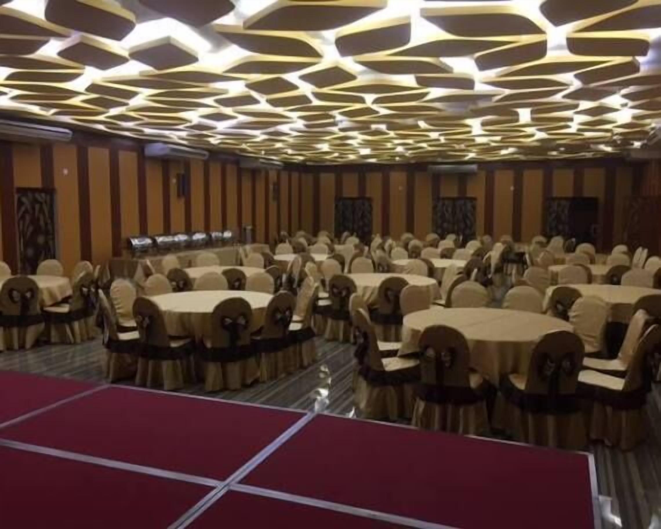 A banquet hall with round tables and chairs, a patterned ceiling, and a red carpet area.