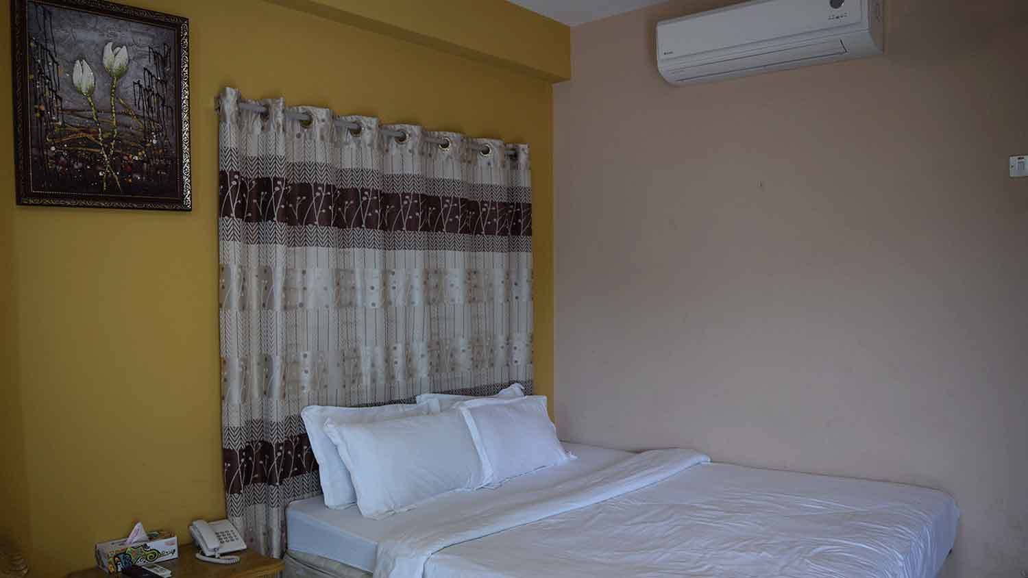 A room with a bed, a telephone, and a painting on the wall.