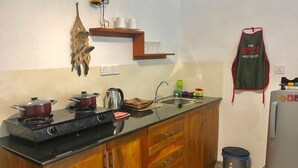 Une cuisine de taille réduite, avec un meuble en bois, un plan de travail noir, une cuisinière, un évier et un réfrigérateur.