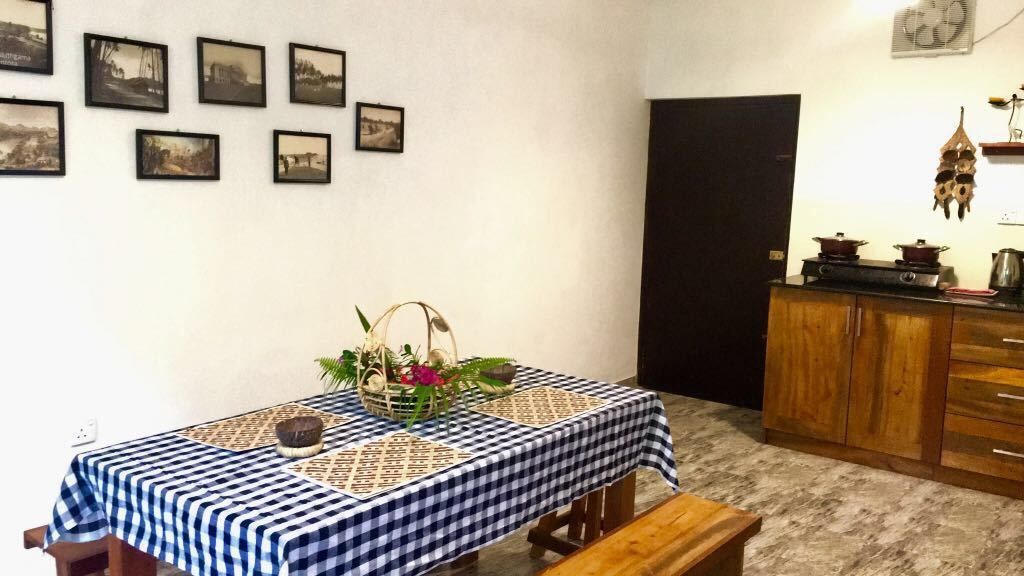 Un comedor con mantel a cuadros, un banco de madera, una cesta con flores y una pared con cuadros.