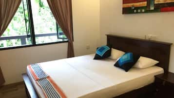 A neatly made bed with a striped blanket and two pillows, a window with curtains, and a painting on the wall.