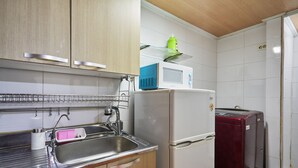 Uma cozinha compacta com pia de aço inoxidável, armários de madeira, micro-ondas e geladeira vermelha.
