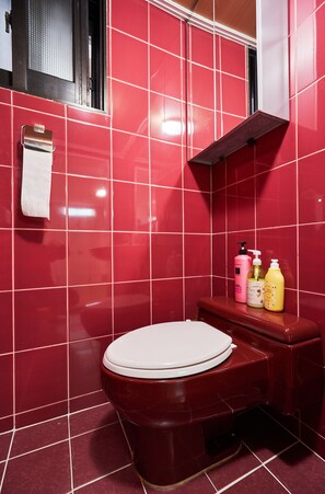 A bathroom with red tiles, a white toilet, and a shelf with toiletries.