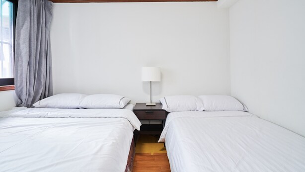 Quarto com duas camas de solteiro, mesa de cabeceira com abajur e janela com cortinas.