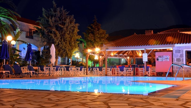 Area piscina notturna con poltrone prendisole e ombrelloni, zona relax coperta e un edificio con tetto in tegole.