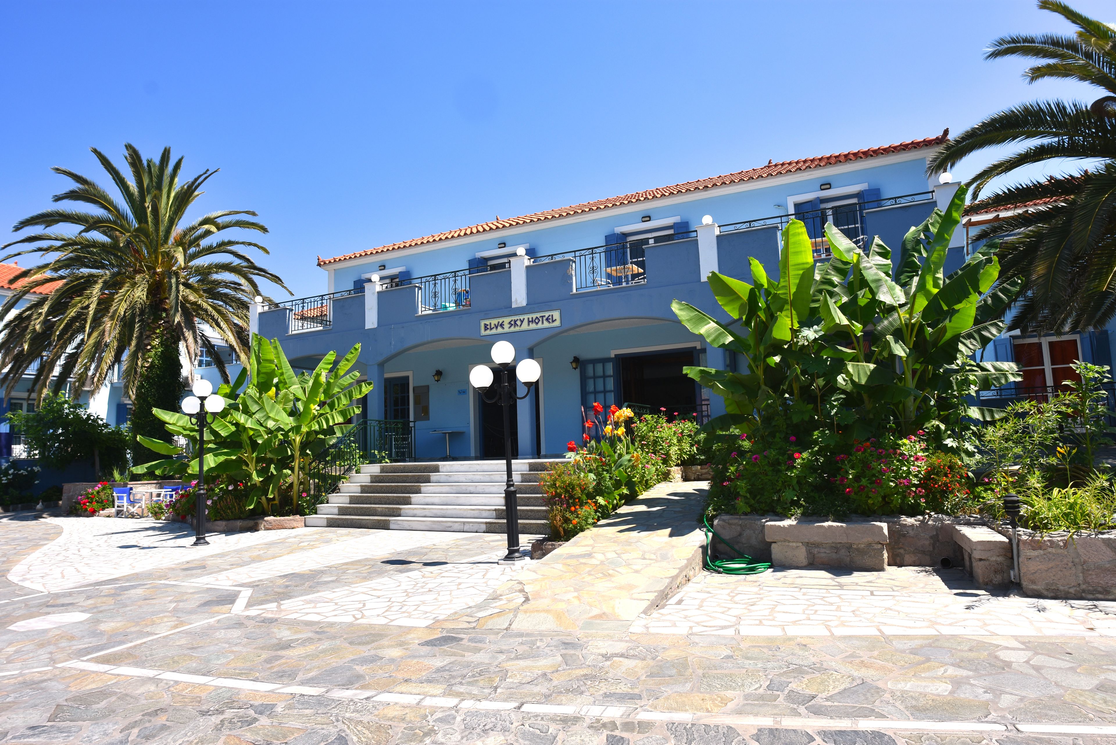 A hotel with a blue facade, a tiled entrance, and a sign reading "Blue Sky Hotel".